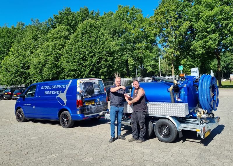 Danny (rechts) geeft een hand naast de bus en de nieuwe blauwe zuigaanhanger