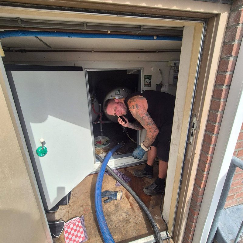 Danny aan het werk in een technische ruimte bij een horecazaak, met de zuigslang naar binnen